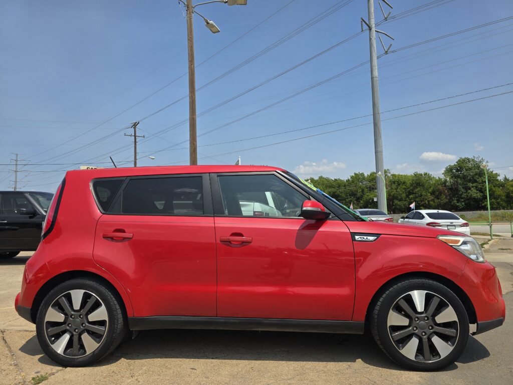 Close-up side view of a bright red SUV parked in a lot with power lines and a clear blue sky behind.