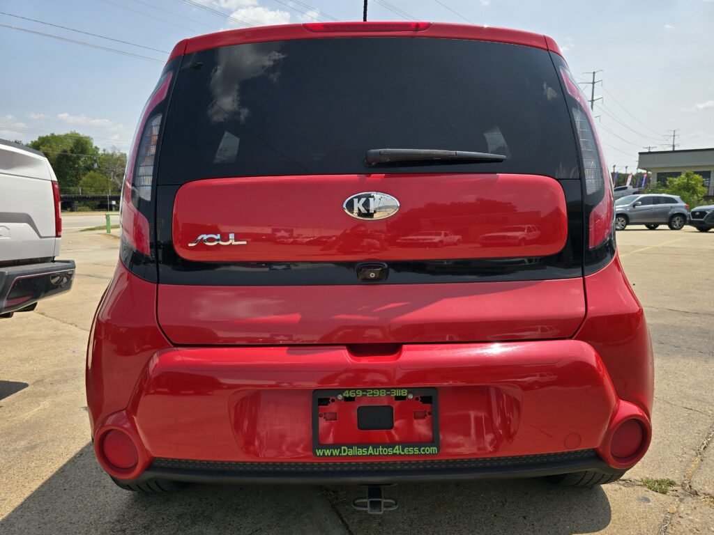 Red Kia Soul seen from the rear in a parking lot, showing the Kia badge and 'Soul' emblem with a DallasAutos4Less.com dealer plate frame.