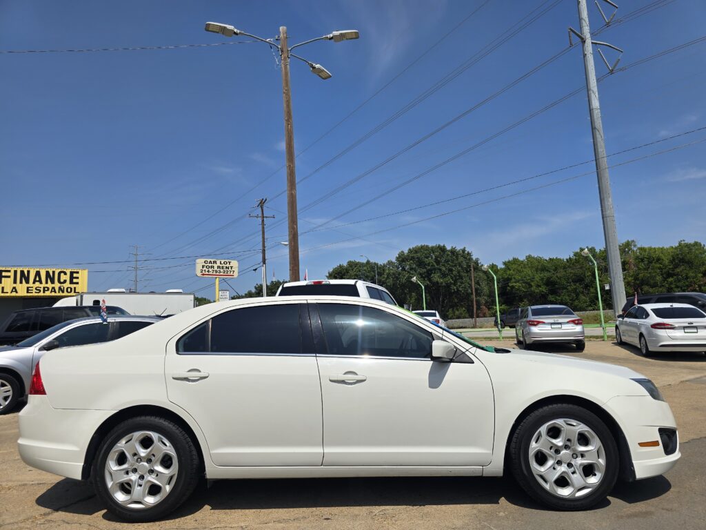 Line of white cars parked in a lot under a clear blue sky with power poles and lines in view.