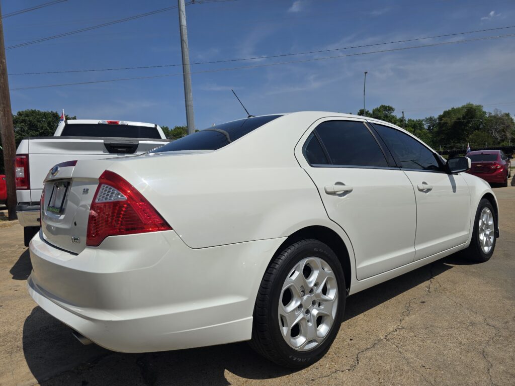 White sedan in foreground in a parking lot with a white pickup behind it and a blue sky above.