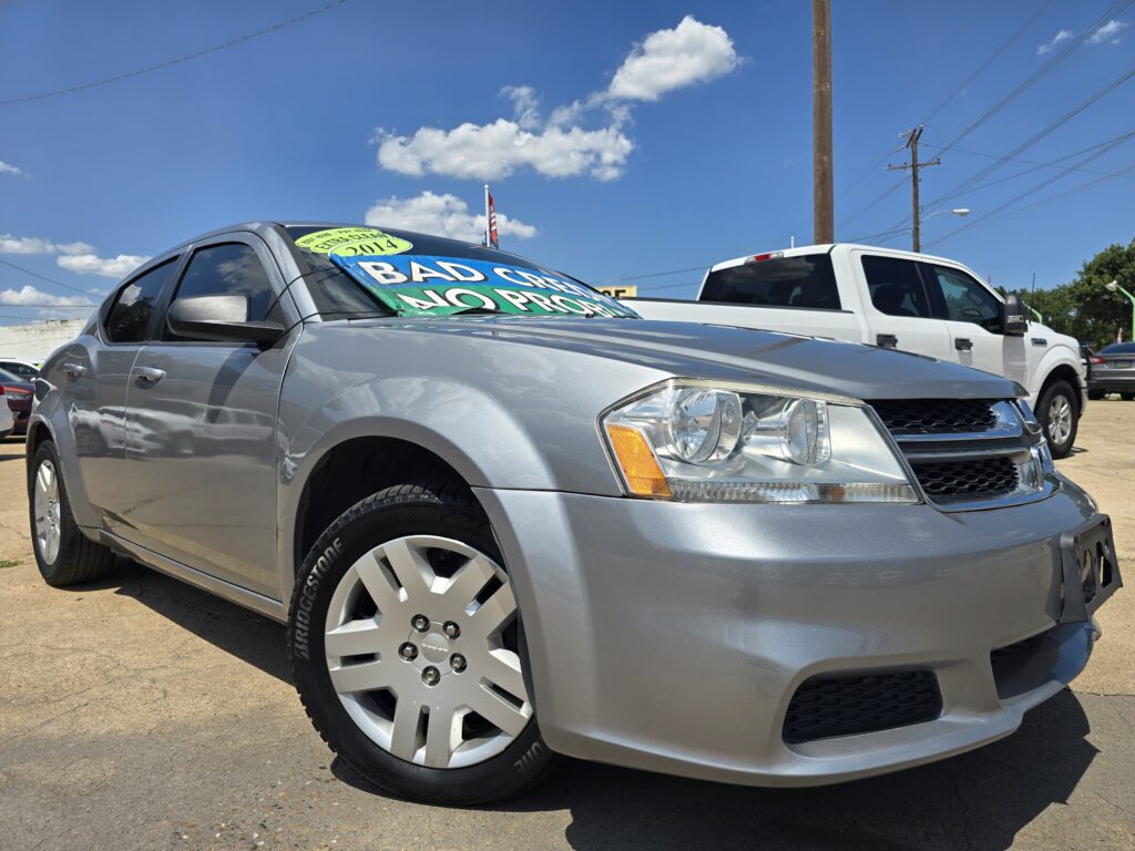 Silver SUV at a car lot with a bright windshield sign reading 'BAD CREDIT NO PROBLEM' and a white pickup in the background under a blue sky.