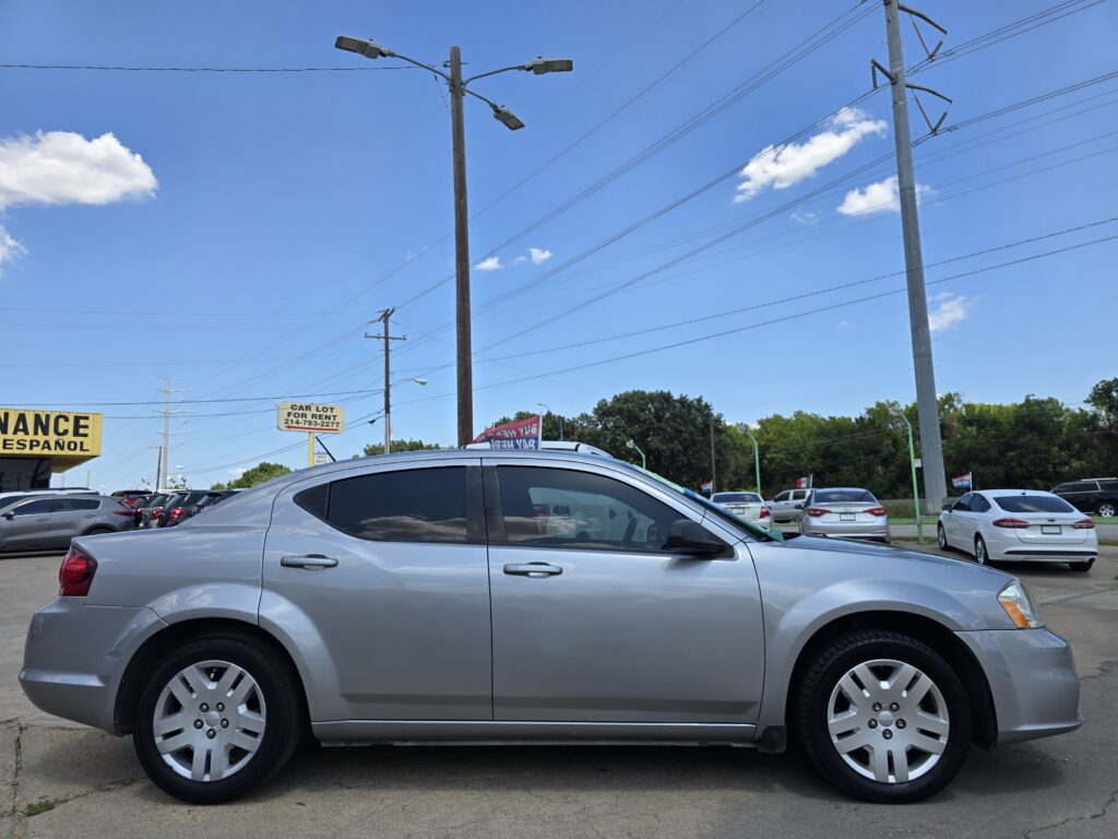Silver car parked in a car lot with other vehicles, power lines overhead, and a blue sky.