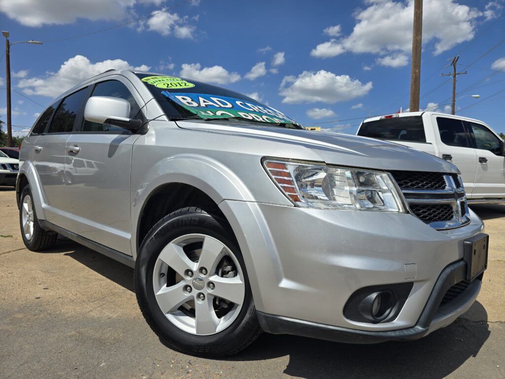 Front-left view of a silver SUV in a car lot with a bright green windshield sign reading 'BAD' and '2012' visible on the glass.