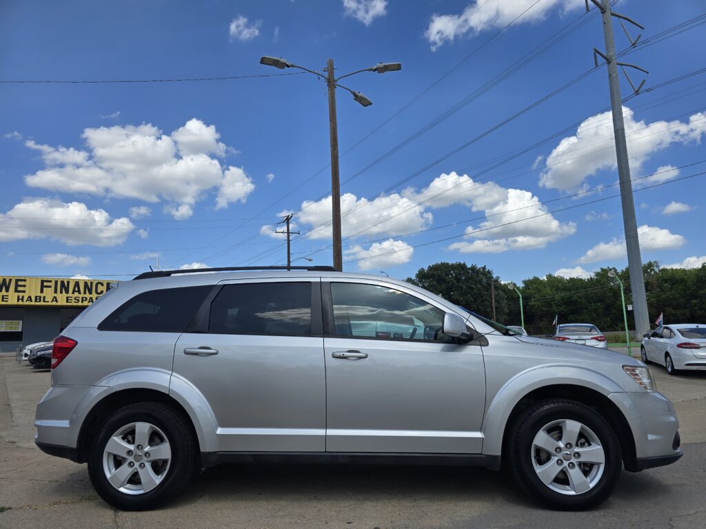 Silver SUV parked in a car dealership lot with a bright blue sky, utility poles, and power lines in the background.