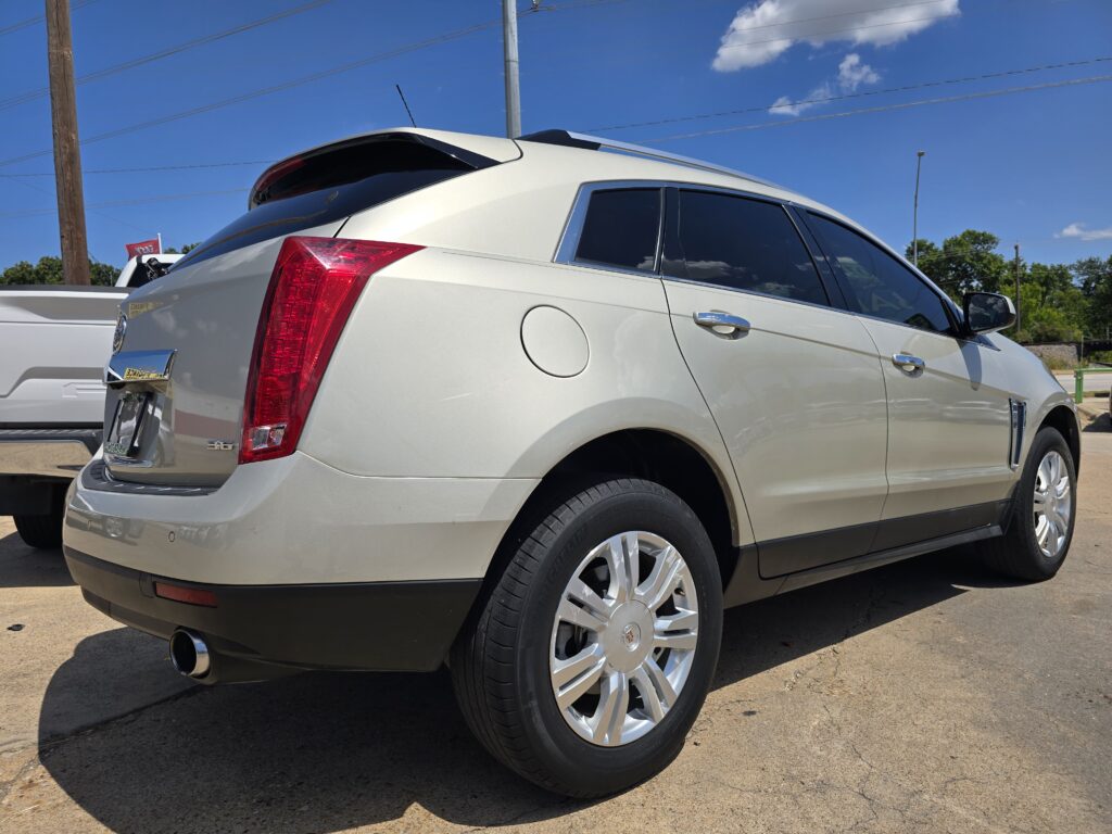 Rear three-quarter view of a white Cadillac SUV with red taillight and chrome trim, parked outdoors on a sunny day.