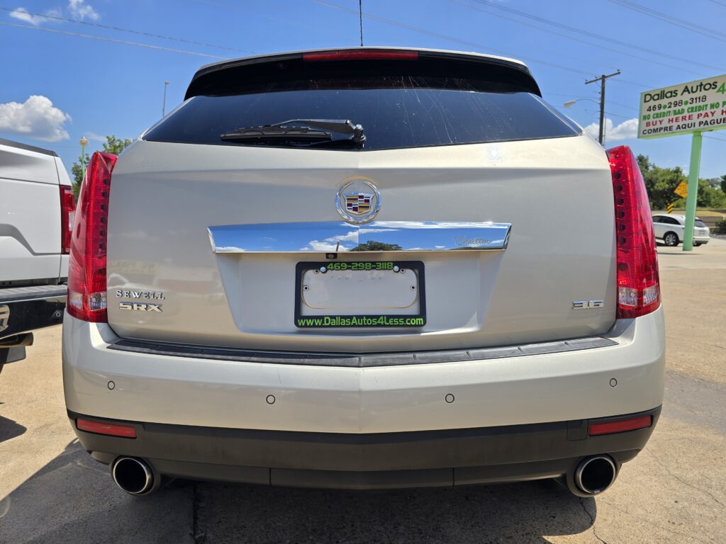 Rear view of a silver Cadillac SUV with dealership plate frame and badge, tail lights visible in a car lot.