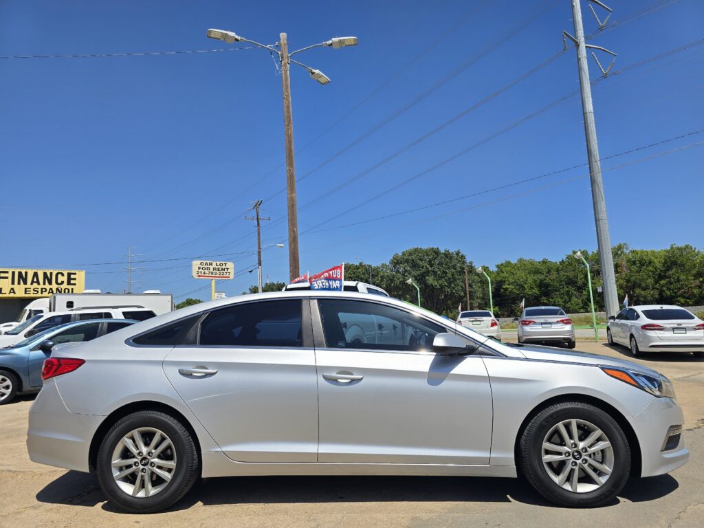 A car dealership lot with several silver and white cars parked under a clear blue sky and utility poles nearby