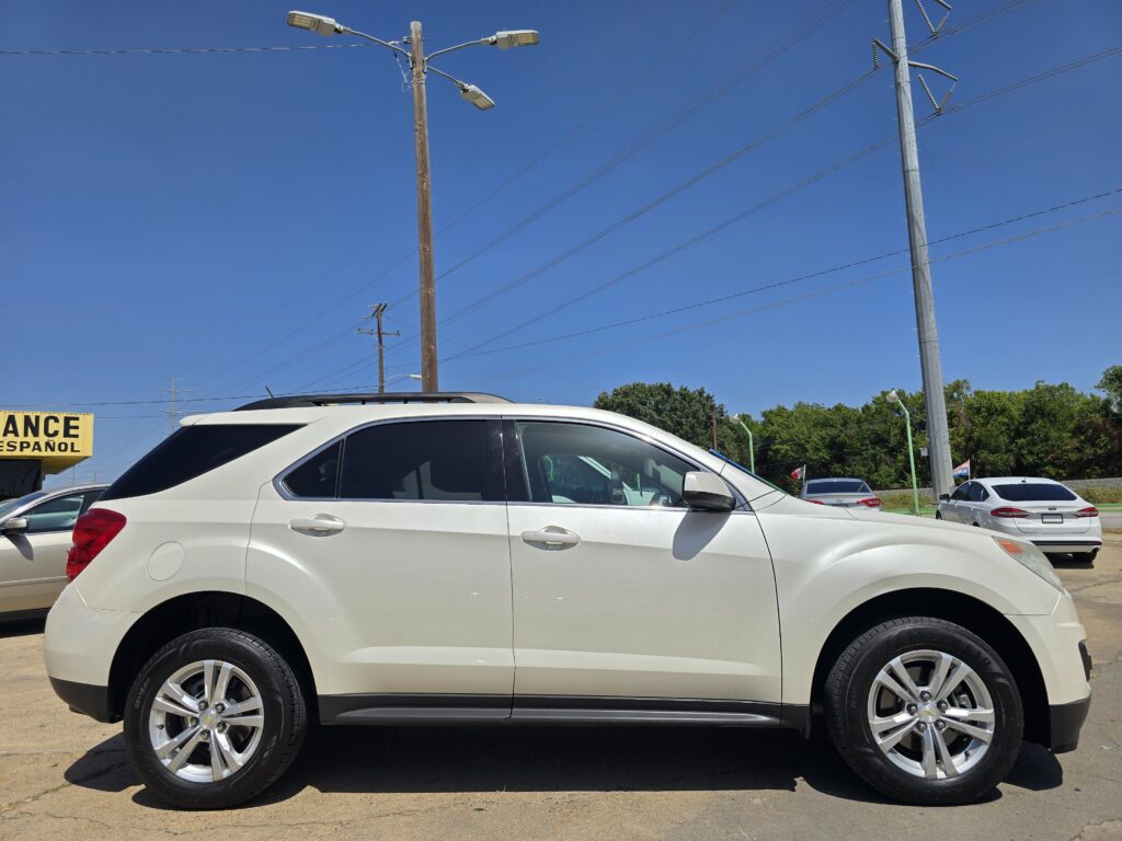White SUV parked in a lot with other cars, under a clear blue sky and overhead power lines; partial yellow sign on left reads 'ANCE ESPANOL'
