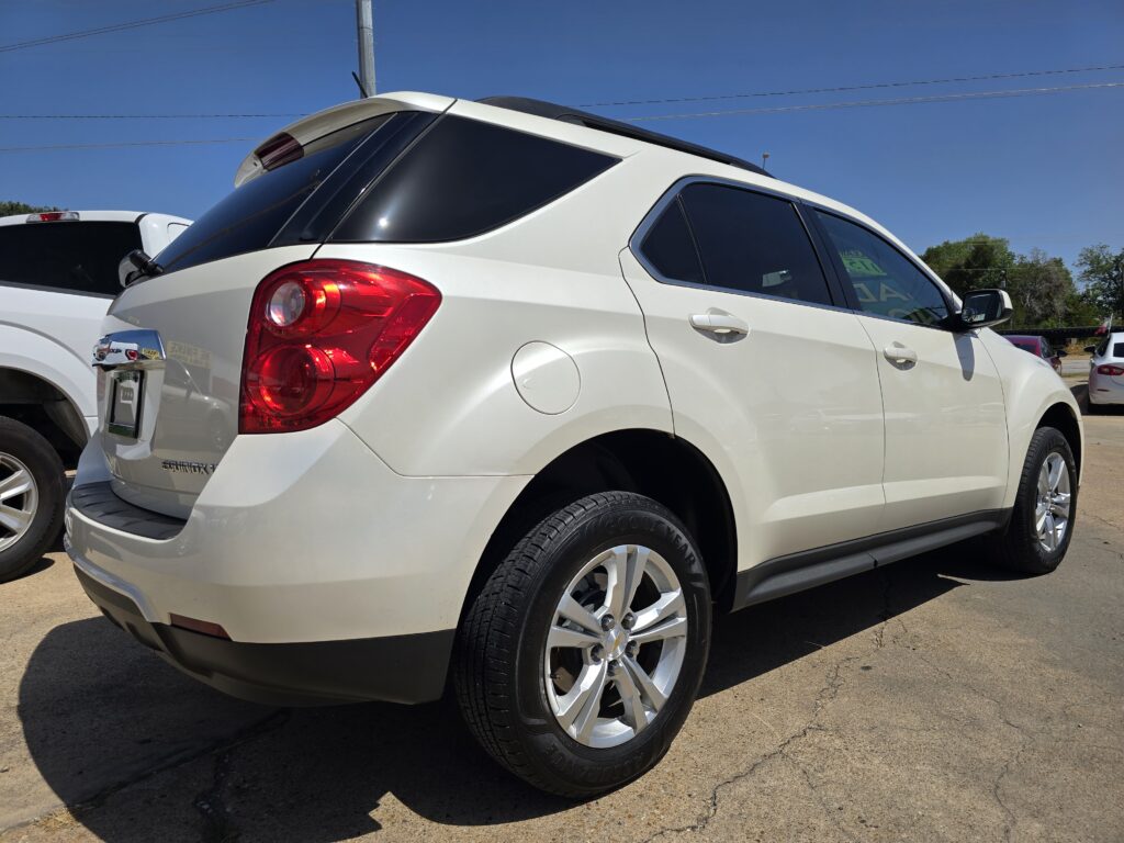Side view of a white SUV in a parking lot on a sunny day, with tinted rear windows and large alloy wheels visible on the curbside.