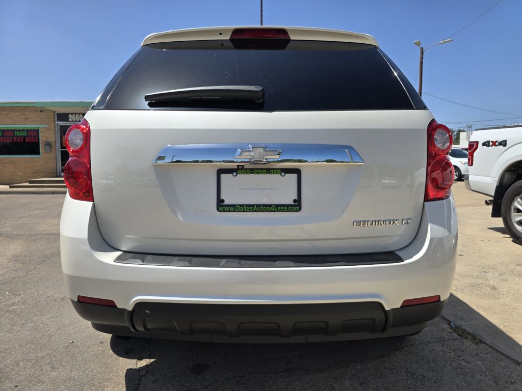 Rear view of a white Chevrolet Equinox LT, with dealer plate frame reading DallasAutos4Less, parked in a lot.
