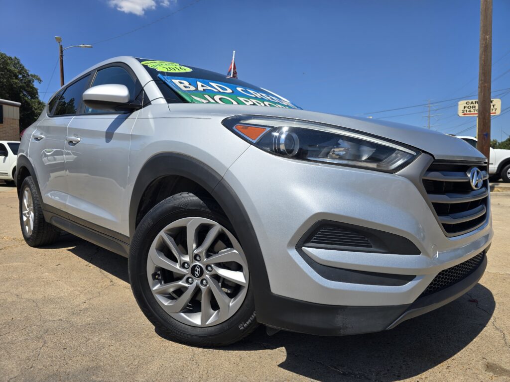 Front-left view of a silver SUV with a large green sale sign on the windshield in a sunny car lot