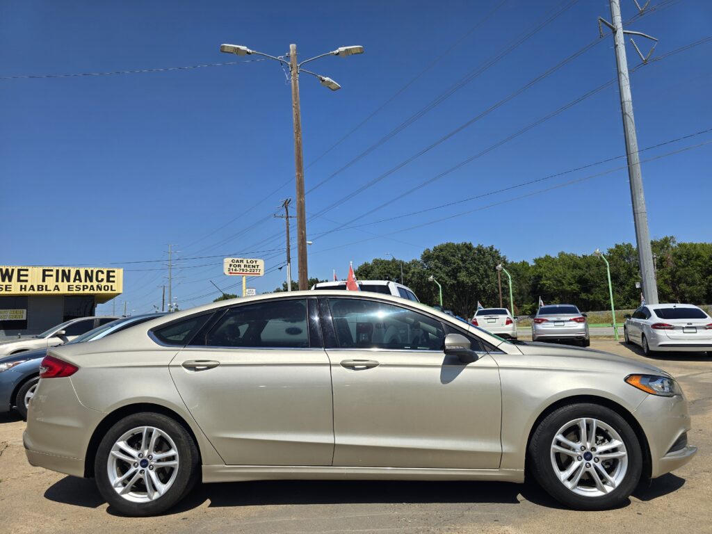 Row of parked silver and white cars in a dealership lot with a yellow 'WE FINANCE' sign on the left and a clear blue sky above.